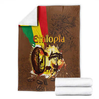 Deep brown Ethiopia blanket folded with flag stripe, coffee-wildlife artwork; stack of towels