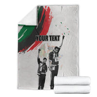 Light gray personalized blanket with green-red brush stripe; folded blankets stacked nearby
