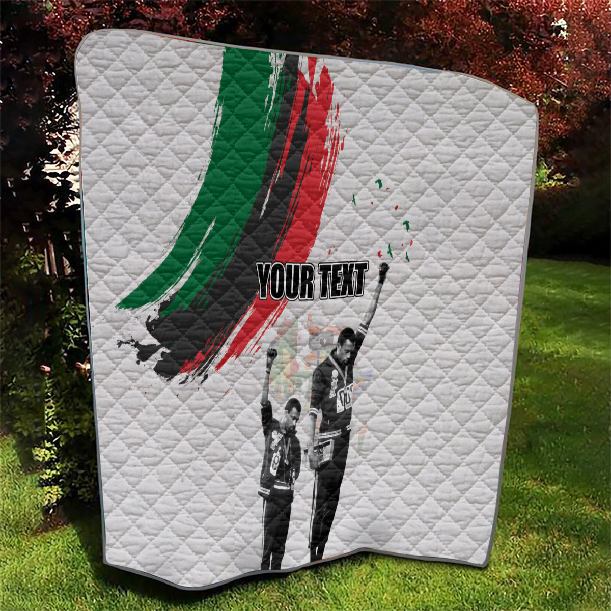White quilt outdoors with green/red brushstroke, black-and-white figure print, 'YOUR TEXT'