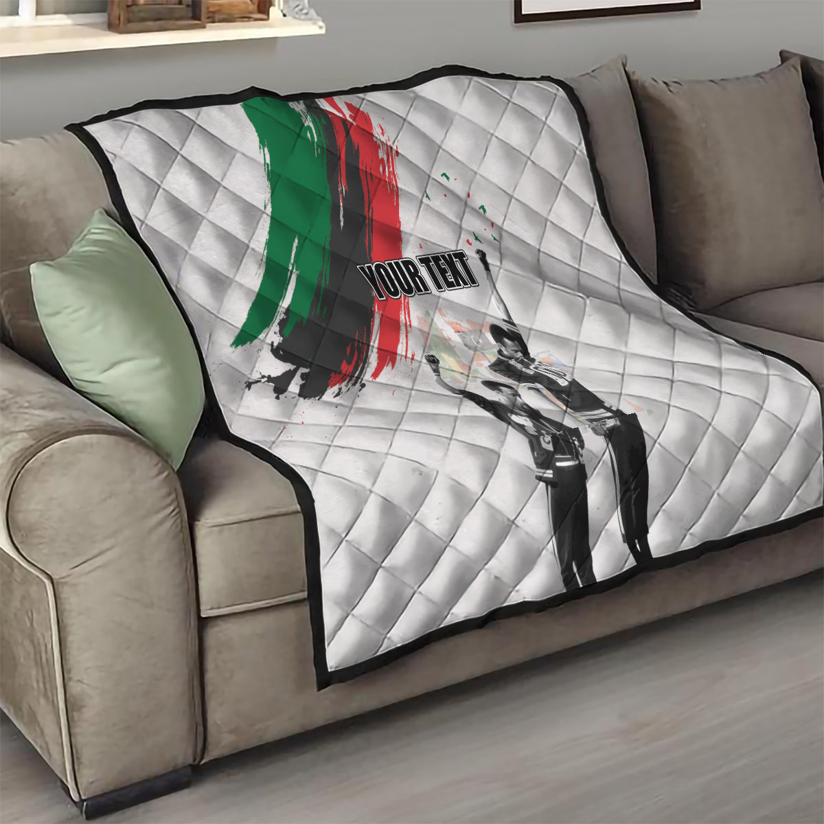 White quilt on gray sofa with green/red brushstroke, black-and-white figures, and 'YOUR TEXT'