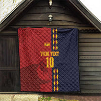 Red and navy quilt blanket with Spain crest, blue/yellow stripes and '10' on wooden wall.