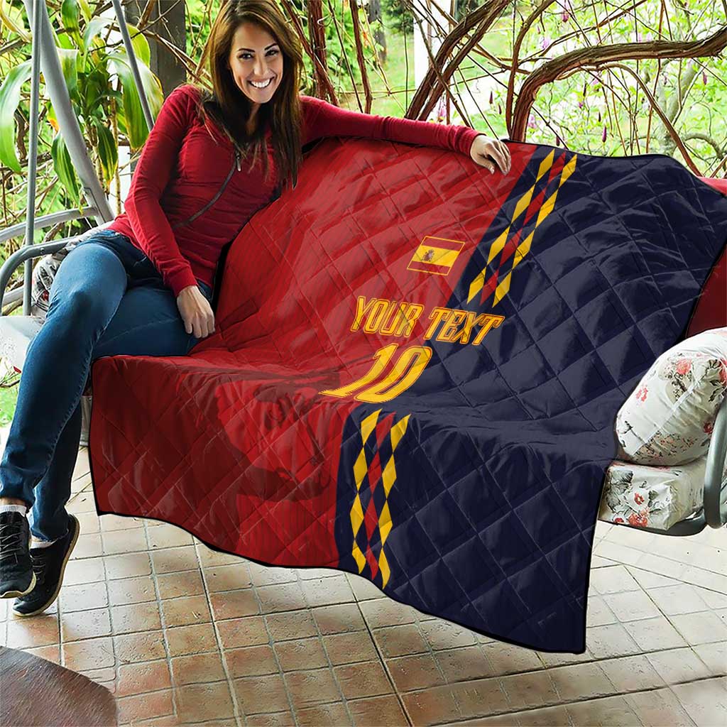 Red and navy diamond-quilt blanket with Spain crest, blue/yellow stripes and '10' held up.