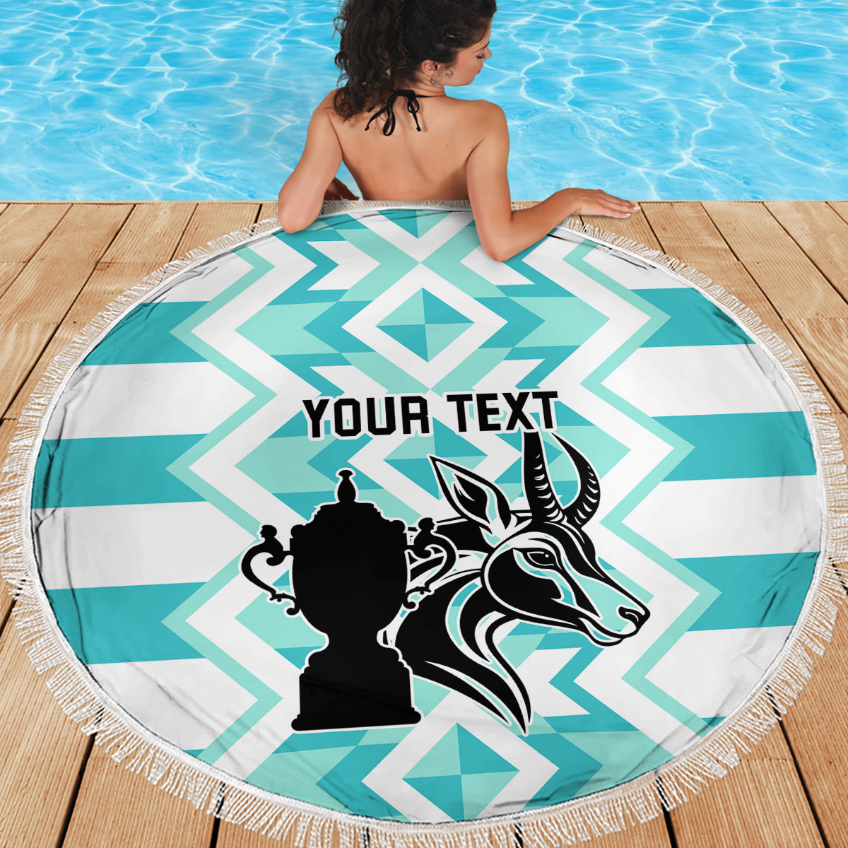 Round beach blanket featuring turquoise-and-white chevrons and black crest, with fringe