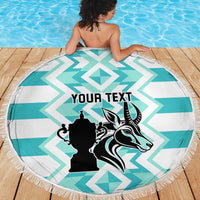 Round beach blanket featuring turquoise-and-white chevrons and black crest, with fringe
