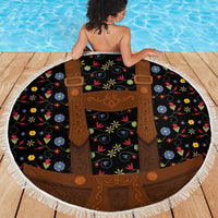 Round floral beach blanket with brown lederhosen apron graphic on black base, white fringe