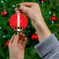 Hand holding red round ceramic Swiss-themed Santa suit ornament with gold string