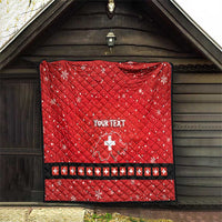 Red quilt with Swiss cross and “YOUR TEXT”, displayed on outdoor wall