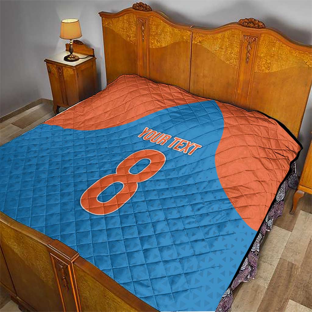 Personalized quilt on a bed in blue and orange with number 8 and “YOUR TEXT”