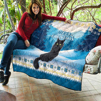 Blue quilt laid over seating with black cat and “Merry Christmas” lettering