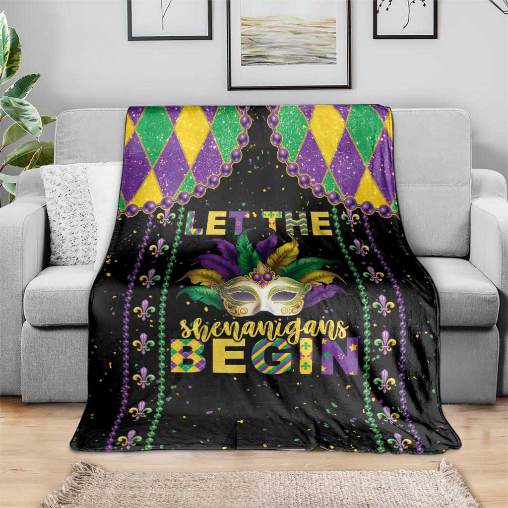 Black Mardi Gras blanket on gray couch with colorful mask, 'Shenanigans Begin' lettering