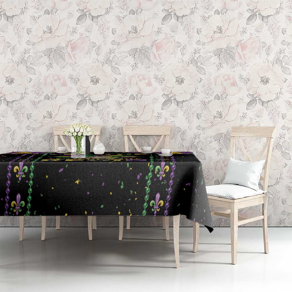Black tablecloth with purple and green fleur-de-lis design and scattered confetti