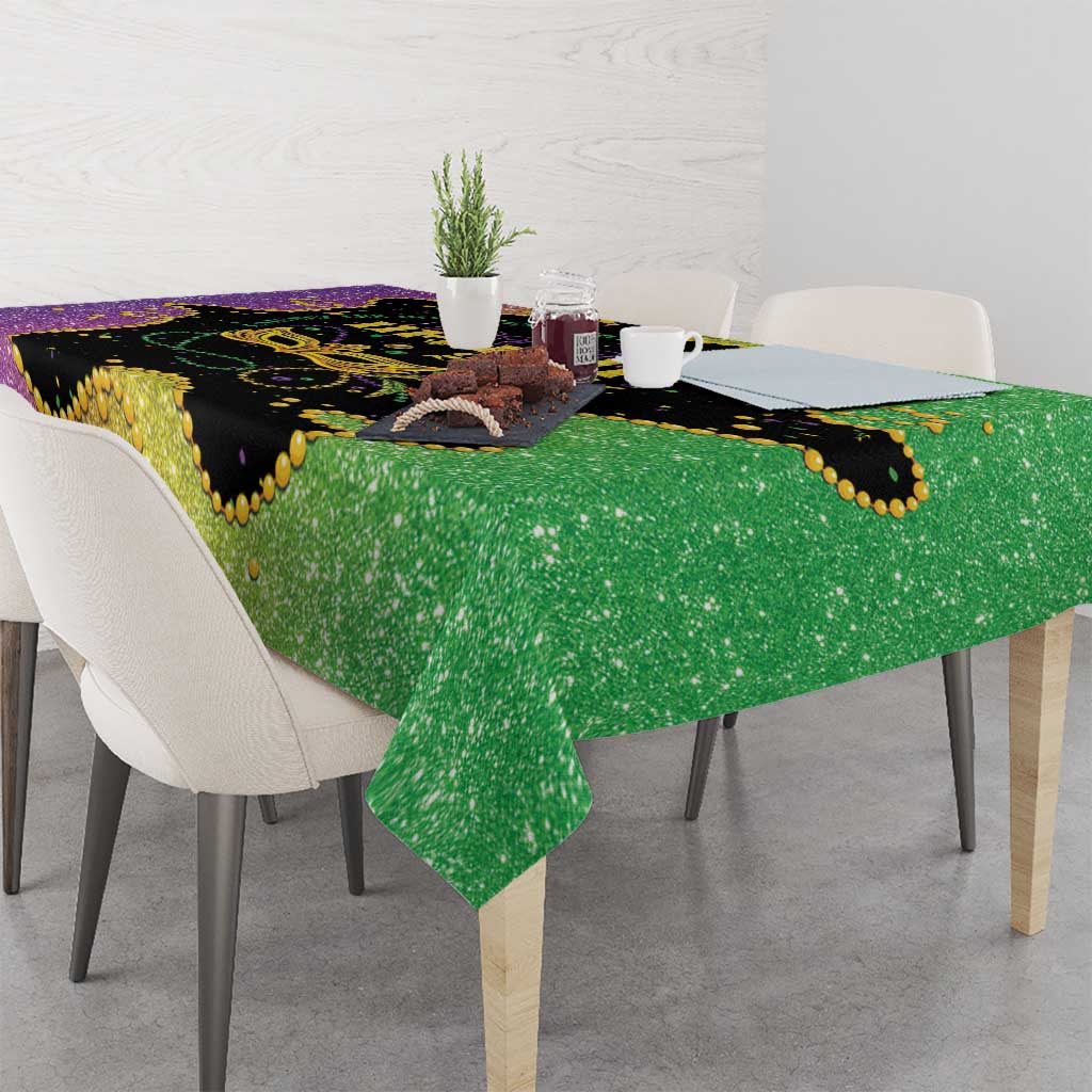 Square Mardi Gras tablecloth draped on table with black, purple, and green glitter design