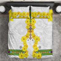 White bedding set with yellow flower cross motif, patterned pillowcases, and colorful border stripe