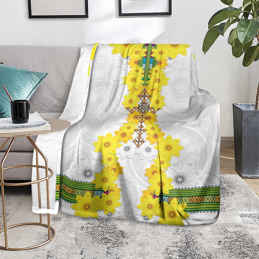 White throw blanket with yellow floral garland and green woven border along the edge