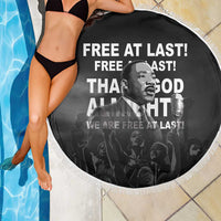 Black round beach blanket with white tassel fringe, MLK portrait and “Free at last” text