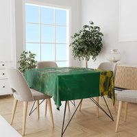 Green tablecloth with yellow patterned border on dining table with chairs