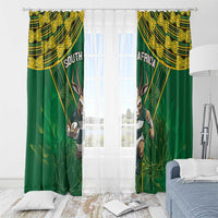 Green window curtains with gold pattern and antelope mascot, with sheer overlay