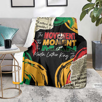 Black MLK legacy blanket with colorful fist artwork and 'The Movement Man' text, on sofa