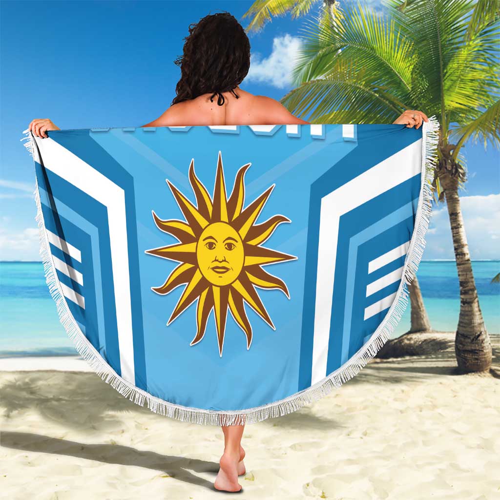 Round blue Uruguay beach blanket with white fringe, sun emblem, held up for display
