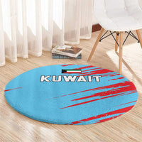 Round blue carpet with red stripe design and KUWAIT text, displayed near a table and chair