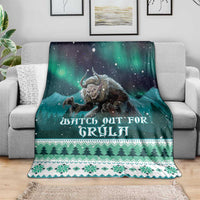 Green Christmas throw blanket draped on sofa, Gryla artwork with trees and snowflake bands
