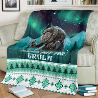 Teal-green Christmas blanket on couch with Gryla face, aurora sky, and pine tree band
