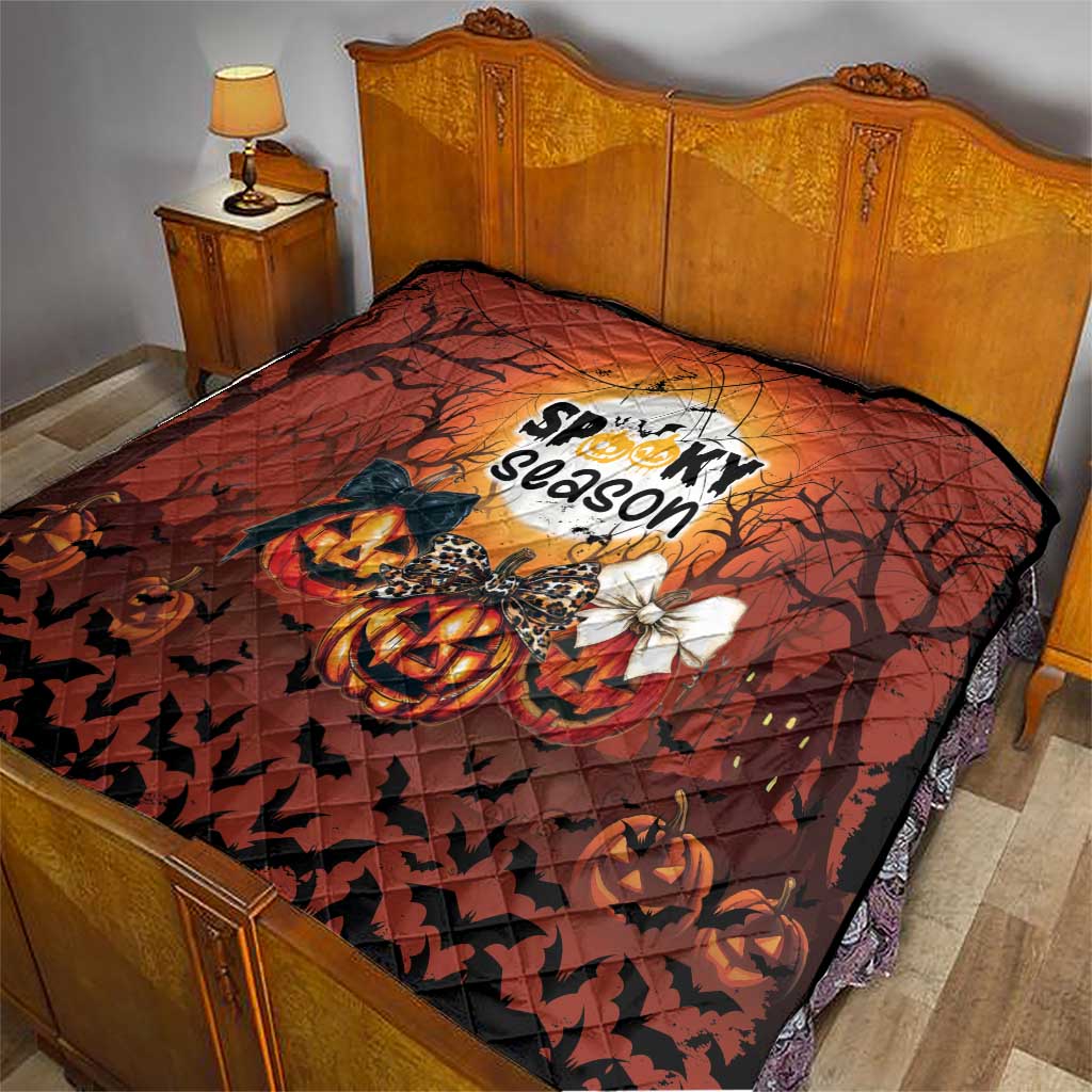 Orange and black Halloween quilt on a bed, featuring jack-o-lantern, bats, and spooky season