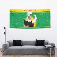 Green Christmas wall tapestry with Ethiopian priest figure above gray couch