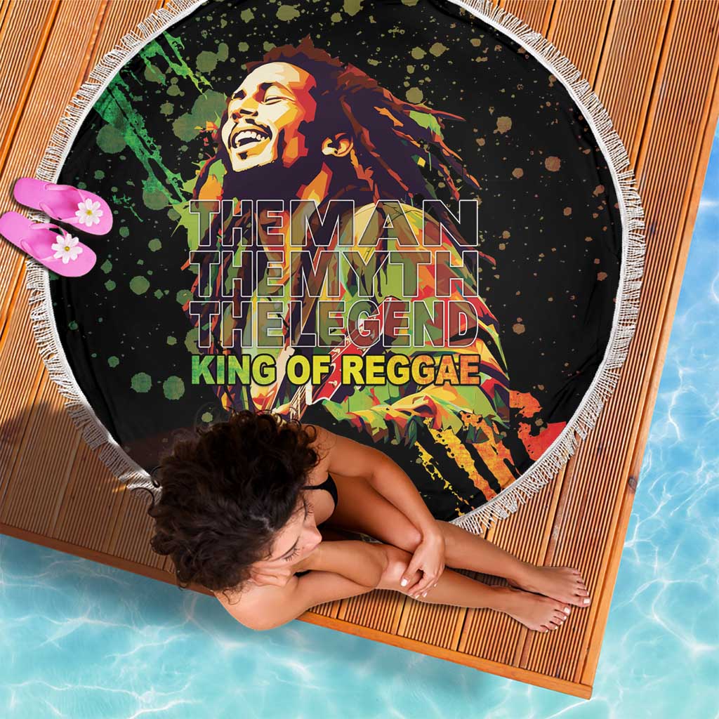 Black round beach blanket, fringed white trim, reggae graphic shown from top angle