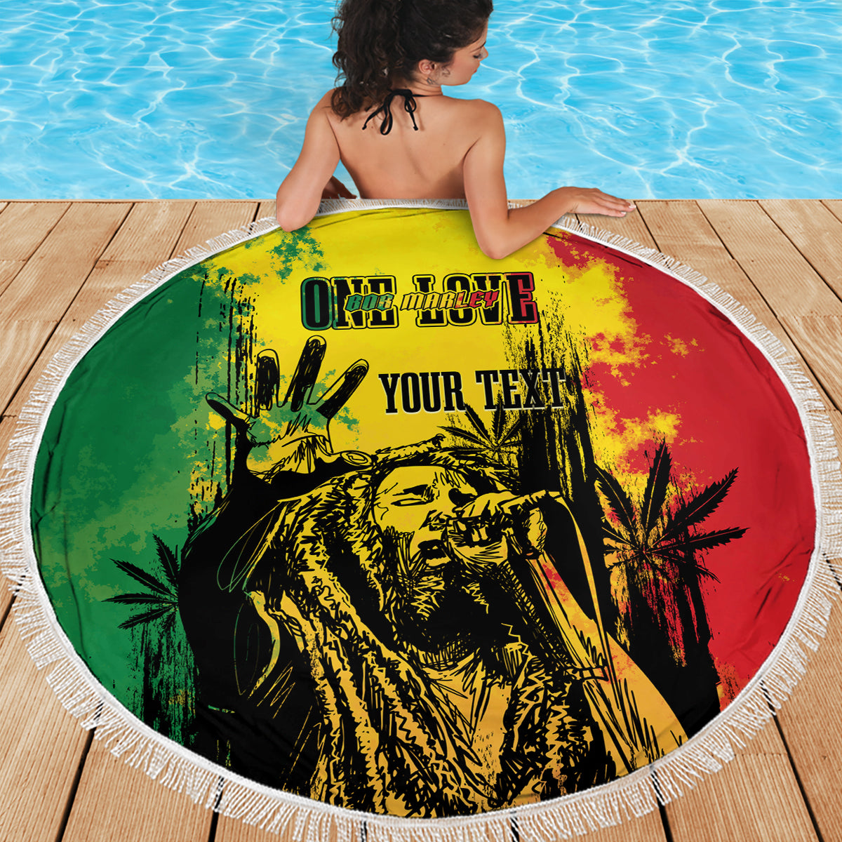 Round fringed beach blanket with reggae grunge "YOUR TEXT" graphic laid on a wooden deck.