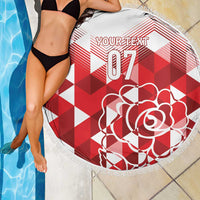 Round beach blanket partially draped, red/white geometric print, rose design, fringe trim