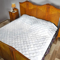 White diamond-quilted quilt covering a bed, with dark edge trim.