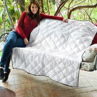 White diamond-quilted quilt draped over a couch, showing black edge trim.