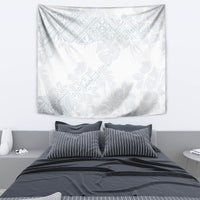 White wall tapestry with light blue tropical floral pattern, shown above a bed.