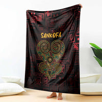 Sankofa heart blanket draped on floor, dark red geometric pattern, gold-green heart emblem