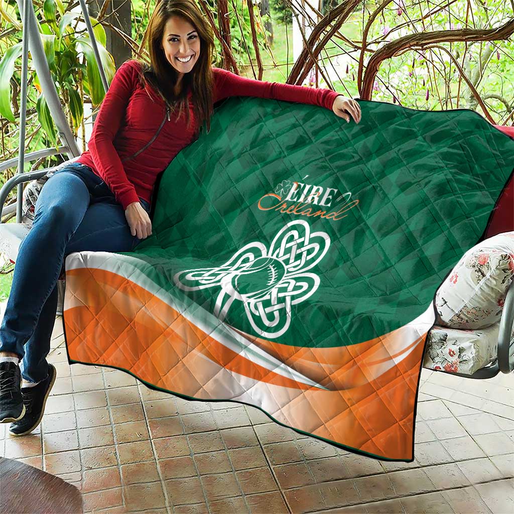 Green quilt blanket with Celtic knot emblem and orange-and-white stripe, spread across couch.