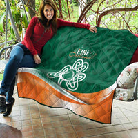 Green quilt blanket with Celtic knot emblem and orange-and-white stripe, spread across couch.