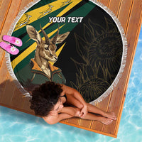 Round beach blanket on a wooden mat with springbok artwork, “YOUR TEXT,” fringed border