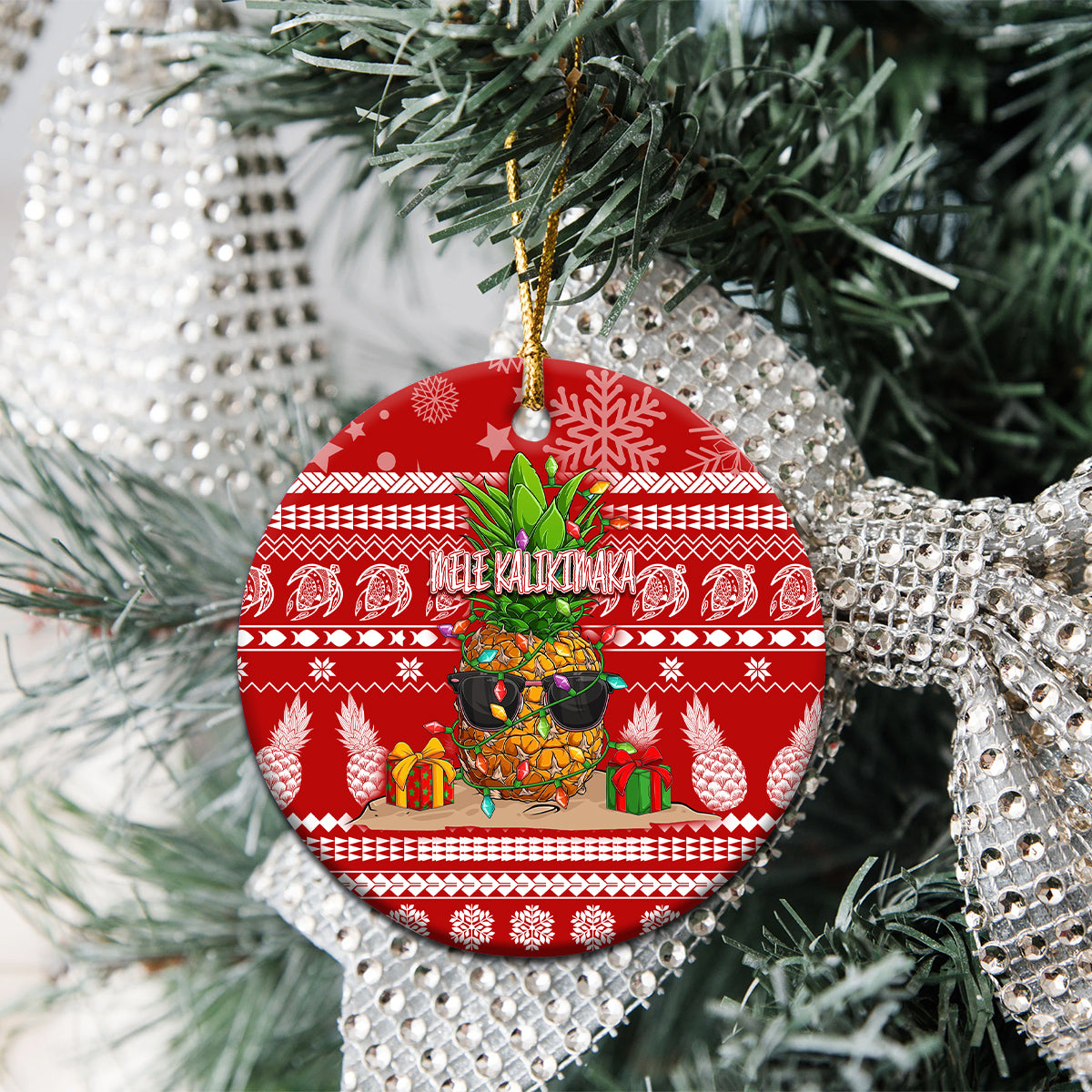 Red ceramic round Christmas ornament with pineapple artwork and hanging gold string on tree