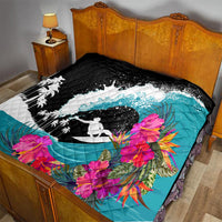 Quilt on a bed: black top, teal ocean field, white wave surfer graphic, pink tropical flowers.