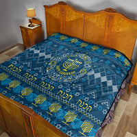 Blue Hanukkah quilt on bed with menorah center, geometric motifs, and yellow lettering