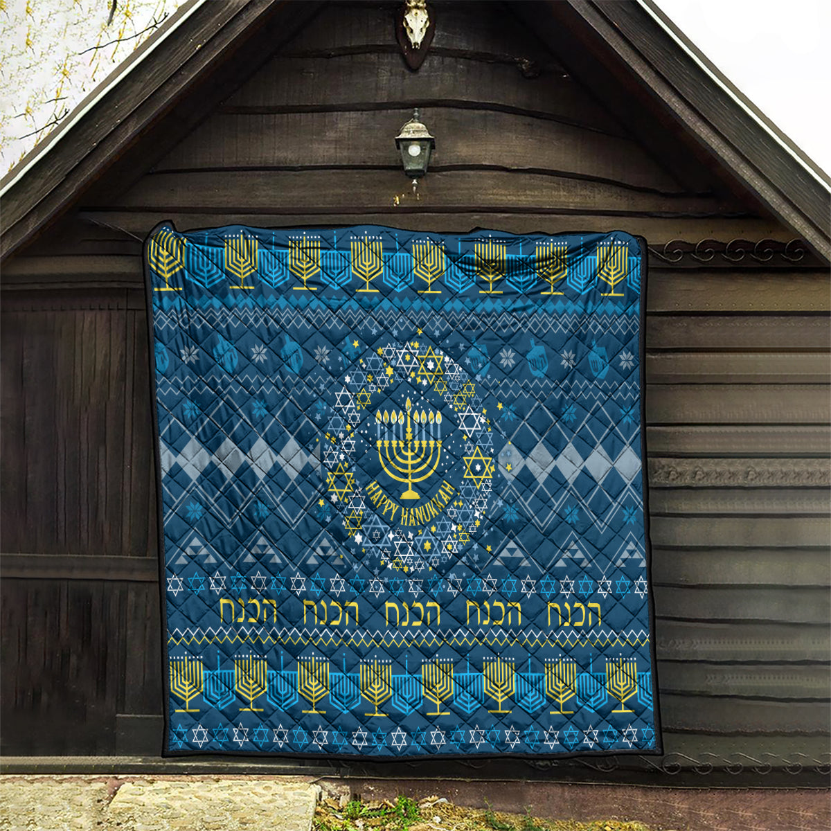 Blue Hanukkah quilt hanging outdoors with menorah star medallion and yellow Hebrew-style text