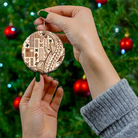 Round beige ceramic tapa ornament with dark pattern, held by a hand with gold hanging loop.