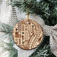 Round beige ceramic tapa ornament with dark pattern, hanging from pine branches with gold loop.