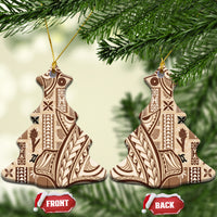 Beige ceramic tapa ornament with dark patterned design, gold hanging loop on pine branches.