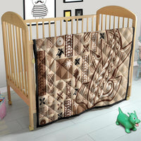 Beige crib quilt with dark brown tapa patchwork and swirl motifs, quilted.
