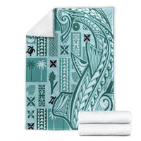 Teal tapa pattern blanket with tribal motifs, neatly folded with white towels beside