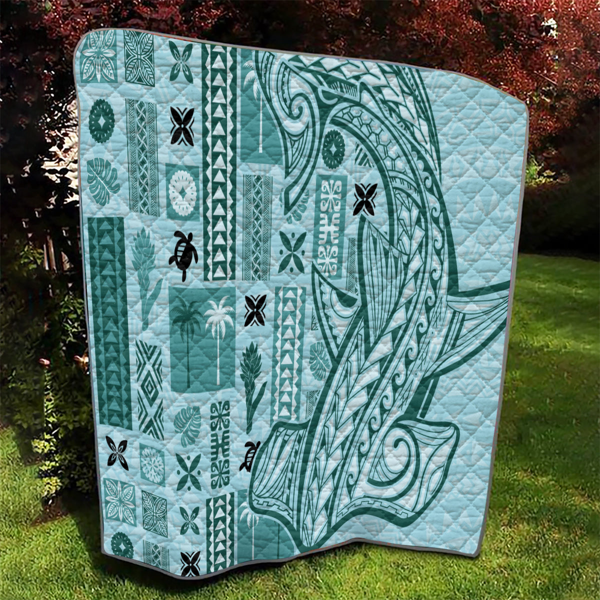 Teal quilt with geometric tapa blocks, swirling tribal motif, and black edge trim