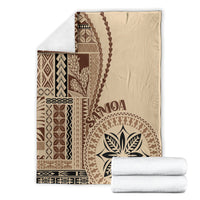 Beige blanket with brown siapo pattern, leaf emblem, and decorative border; folded with stacks