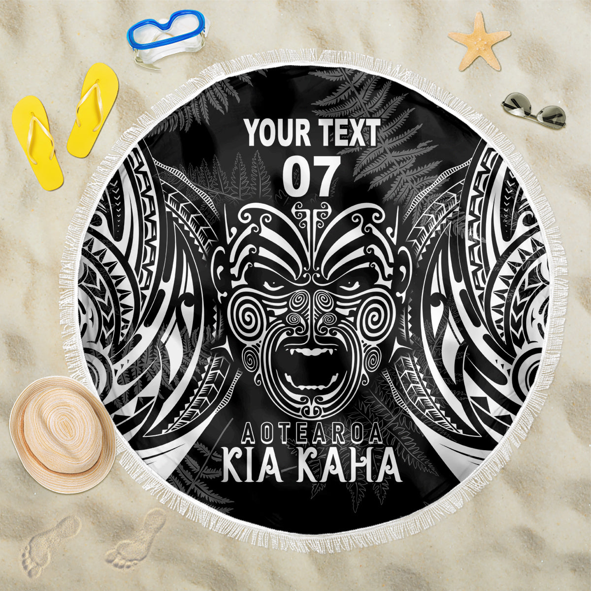 Black round beach blanket with Maori-style face graphic and white fringe border